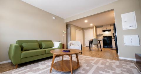 Modern living room with a green sofa, round coffee table, and open kitchen area.