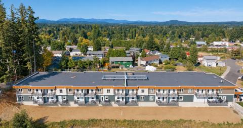 Aerial view of a modern residential building surrounded by trees and houses, under a clear blue sky.
