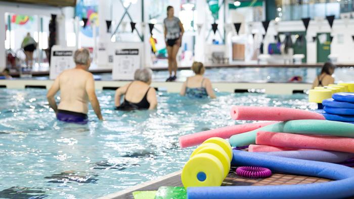 Three people in shallow end of main pool doing aquatic fitness led by an instructor