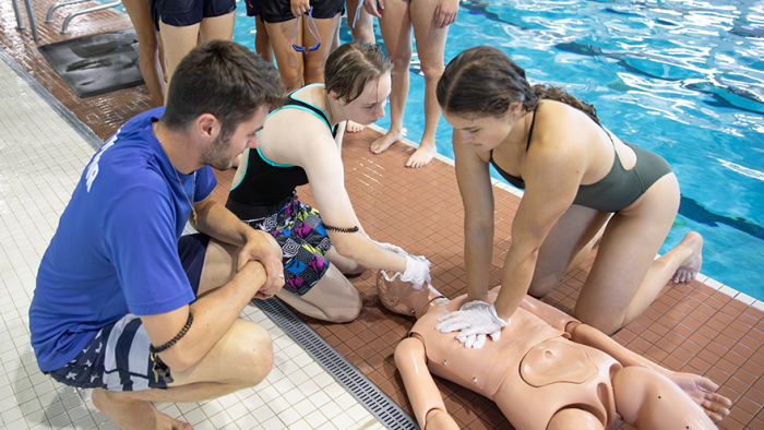 A group of lifeguards in training on the pool deck learning how to do CRP