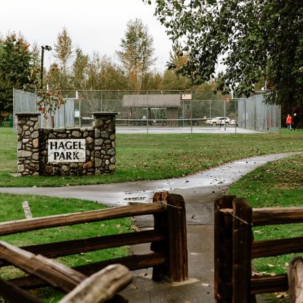 Park entrance with wooden fence, path, and trees on an overcast day.