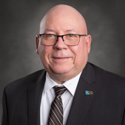Man in a suit and tie, smiling against a gray background.