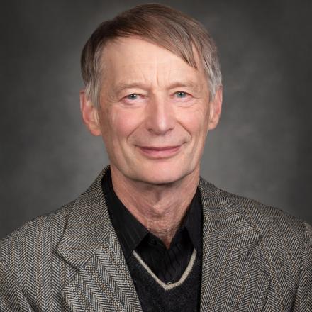 Smiling person in a grey suit with a grey background.
