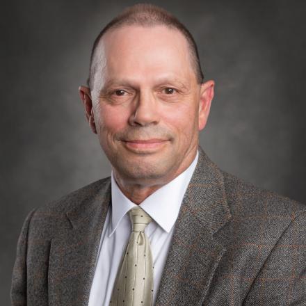 Professional headshot of a person in a suit with a neutral background.