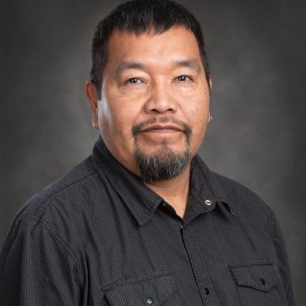 Man in a black shirt with short hair and beard on a gray backdrop.