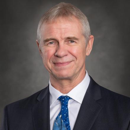 Smiling person in a suit with a blue tie against a grey background
