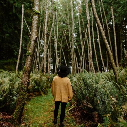 Person in a yellow coat walking through a dense forest path.