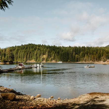 Lake with wooden dock, surrounded by forest under a partly cloudy sky.