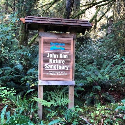 Wooden sign for a nature sanctuary surrounded by lush green forest.