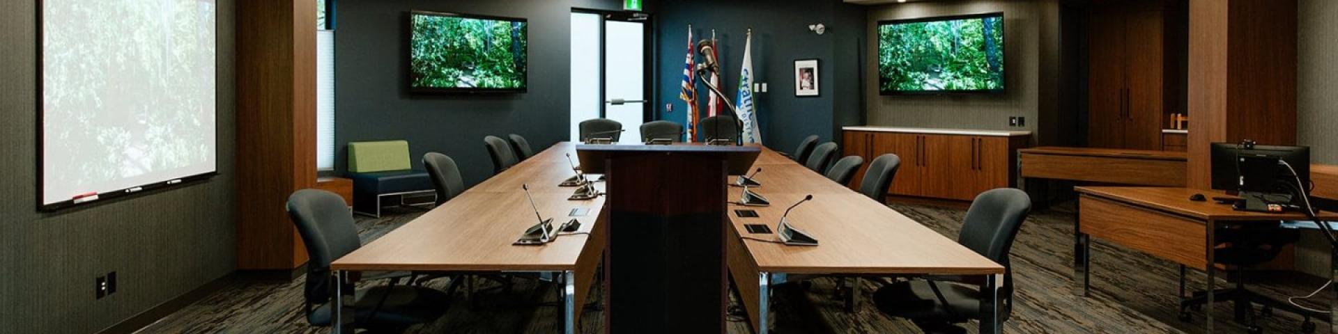 Modern conference room with long tables, chairs, and screens displaying nature scenes.