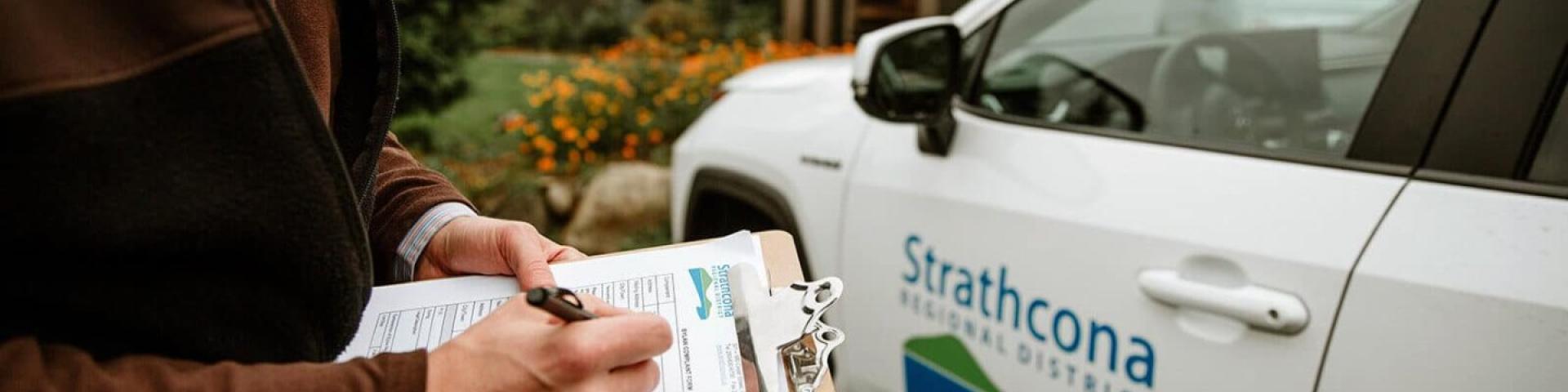 Person writes on clipboard beside a Strathcona Gardens vehicle.