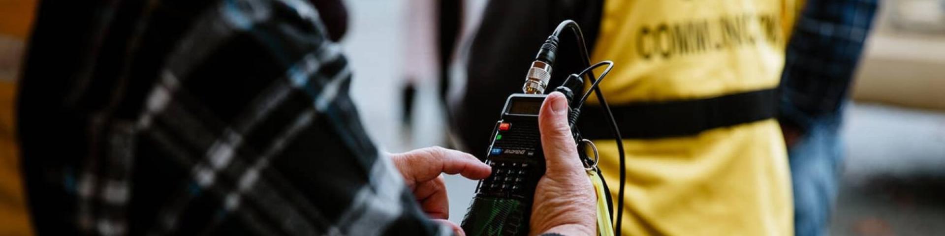 Person in plaid holding a communication device next to people in yellow vests.
