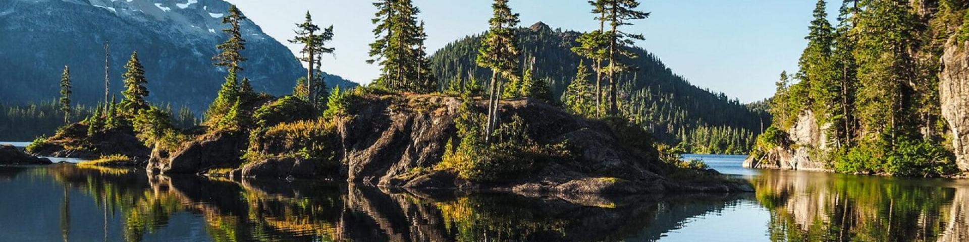 Calm lake reflecting pine trees and snow-capped mountains.