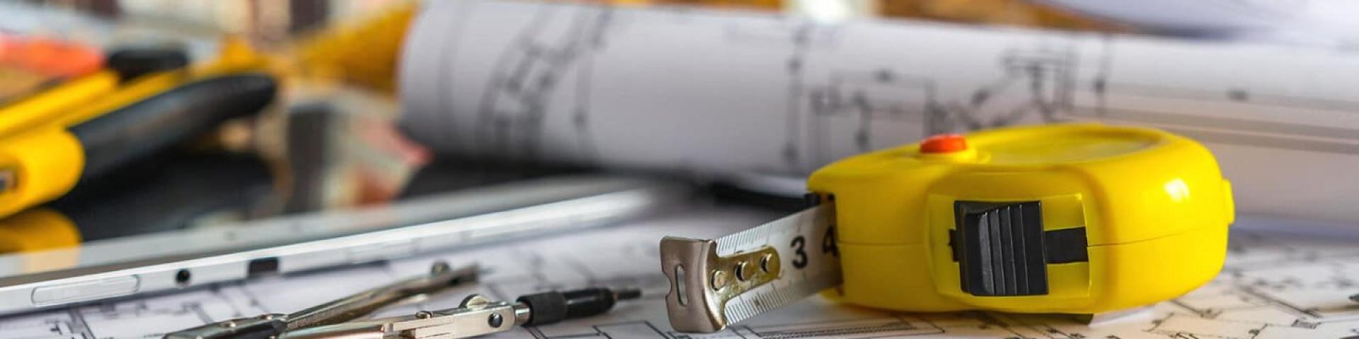 Tape measure and compass on architectural blueprints.