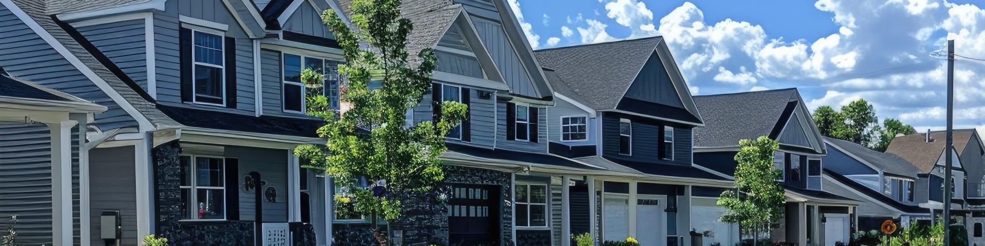 street with houses and trees, under a blue sky with clouds.