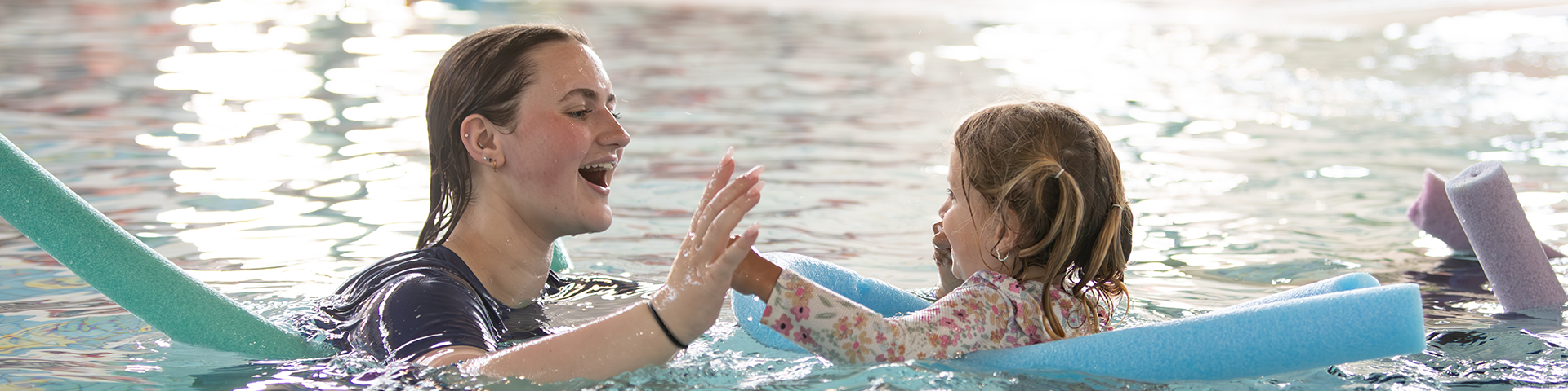 Lifeguard instructor giving a toddler a high five in the pool