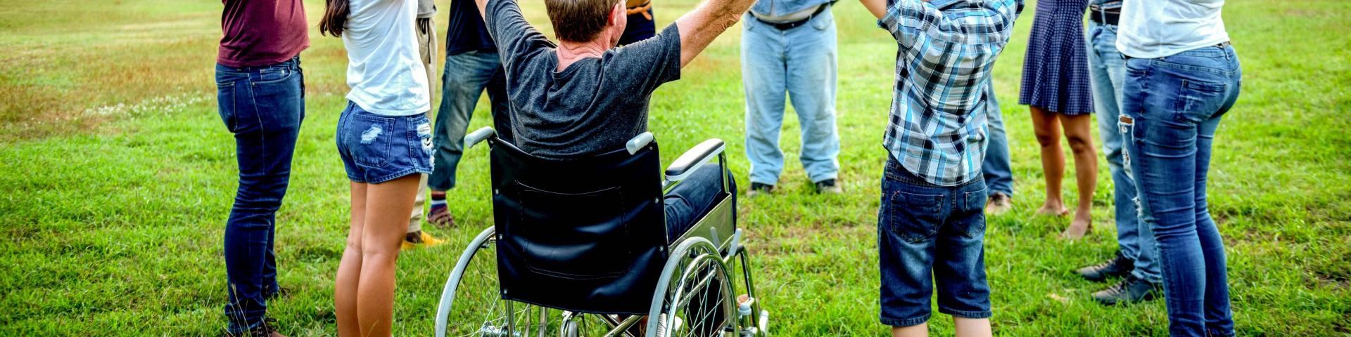 A diverse group of people joyfully holding hands in a circle, with one person in a wheelchair.