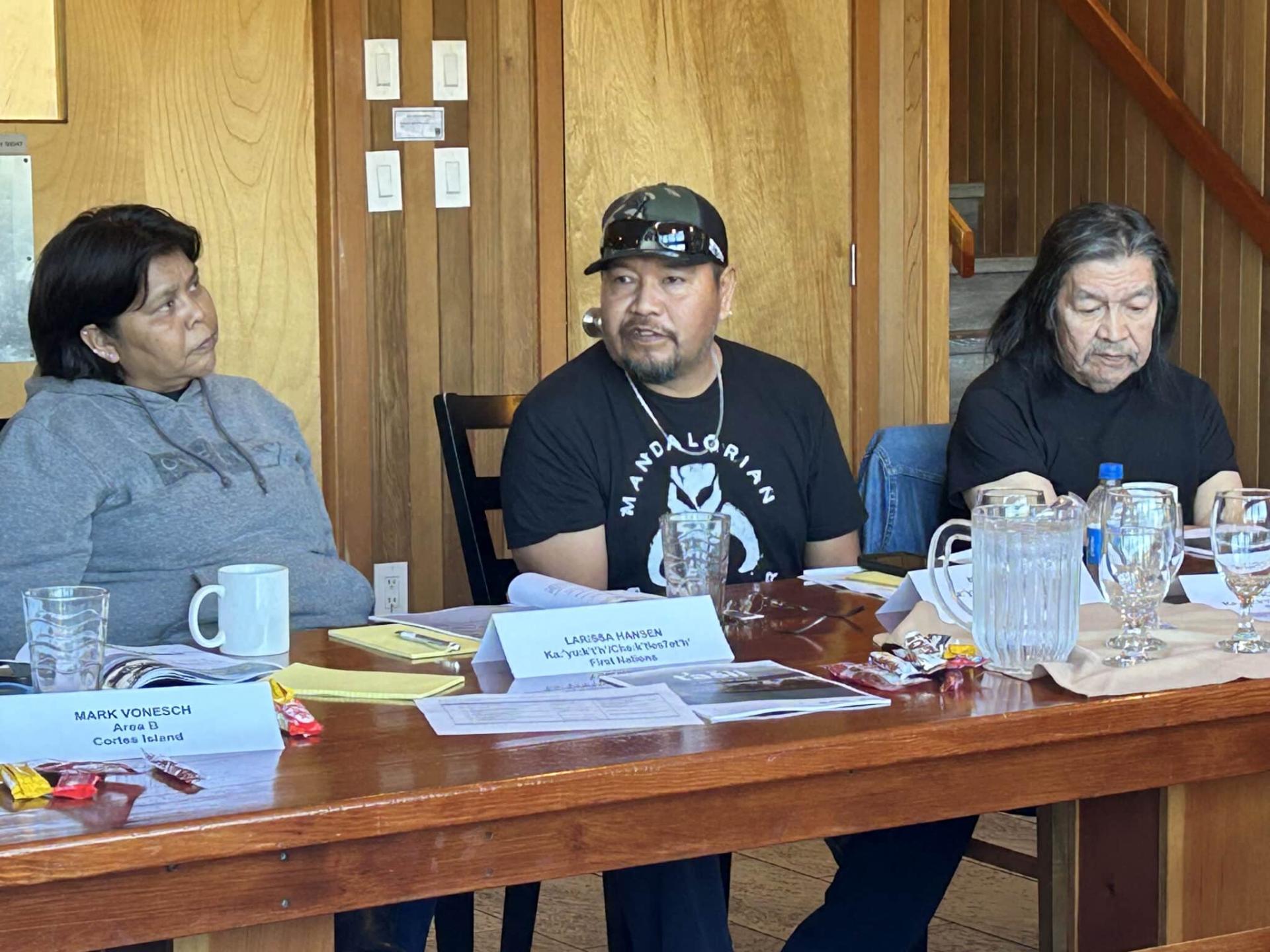 Three people sitting at a wooden table with papers and cups.