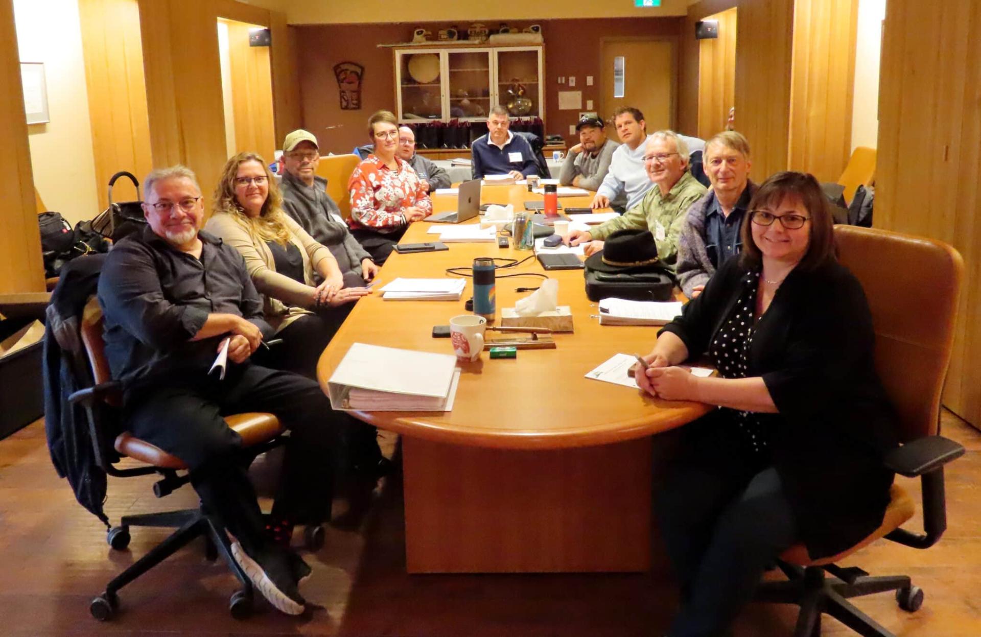 Meeting with people seated around a large wooden table, smiling and attentive.